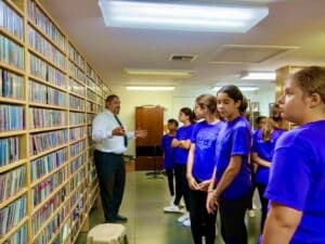 Young girls in GEM program listen to a mentor explaining WDNA’s vast CD library, representing history, culture, and music legacy.